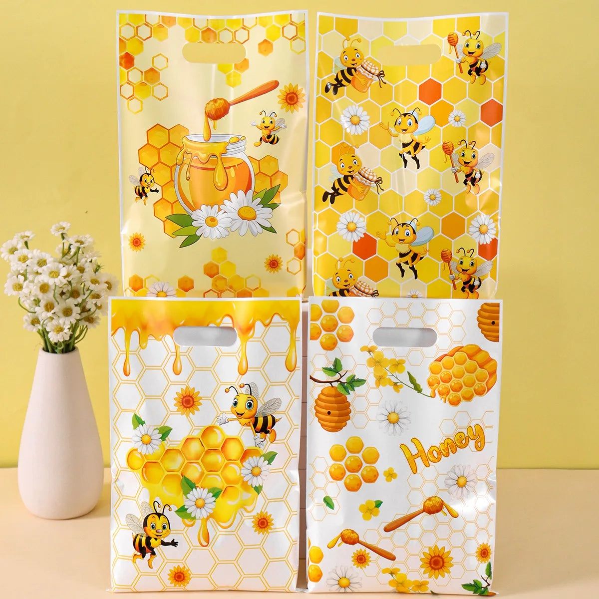 Three clear honey gift bags with yellow and orange bee designs and handles displayed on a light surface.