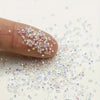 A finger is holding and scattering multicolor AB glass micro beads onto a white surface for nail art or DIY crafts.