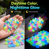 Hands display glow-in-the-dark luminous pebbles under light, showing daytime color and nighttime glow.