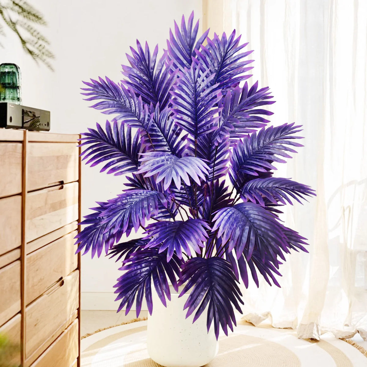 A vibrant purple artificial palm tree with silk leaves displayed in a white vase next to wooden drawers.
