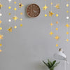 A decorative garland featuring gold and silver stars and polka dots hangs against a gray wall above a clock.