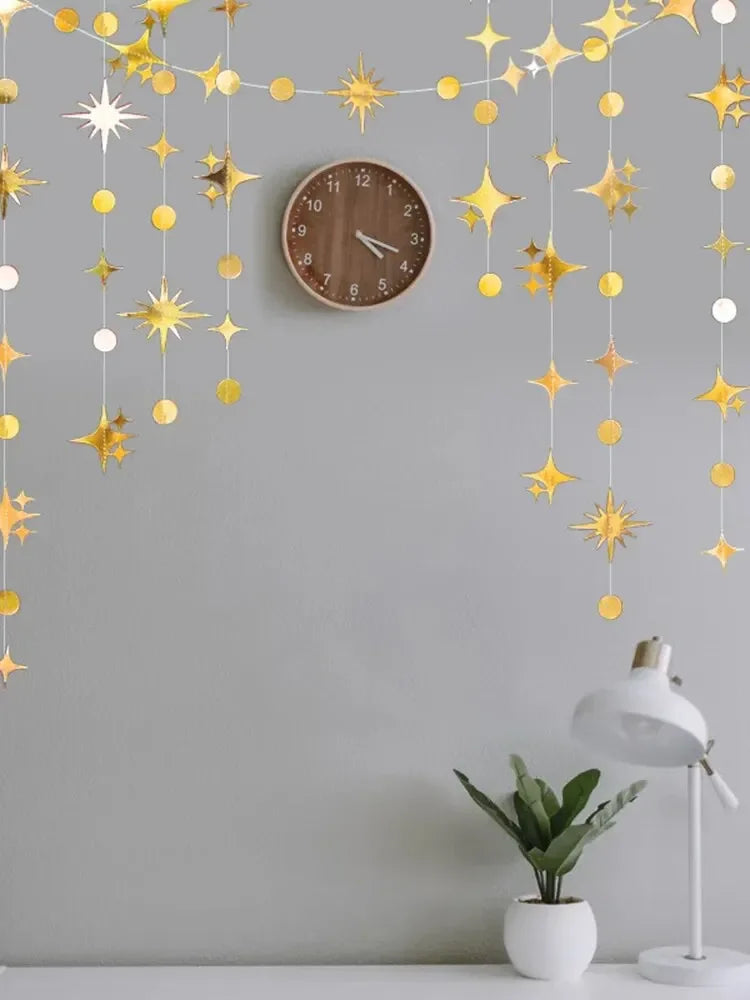 A decorative garland featuring gold and silver stars and polka dots hangs against a gray wall above a clock.
