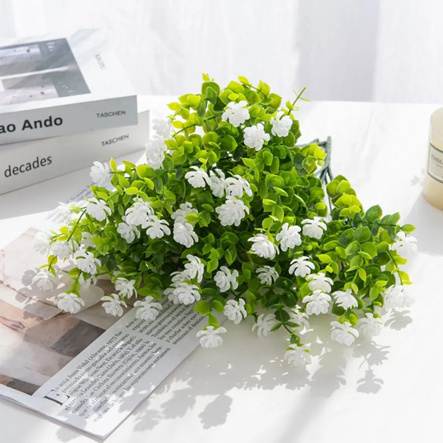 A vibrant green faux plant with white flowers and leaves displayed on a white surface.