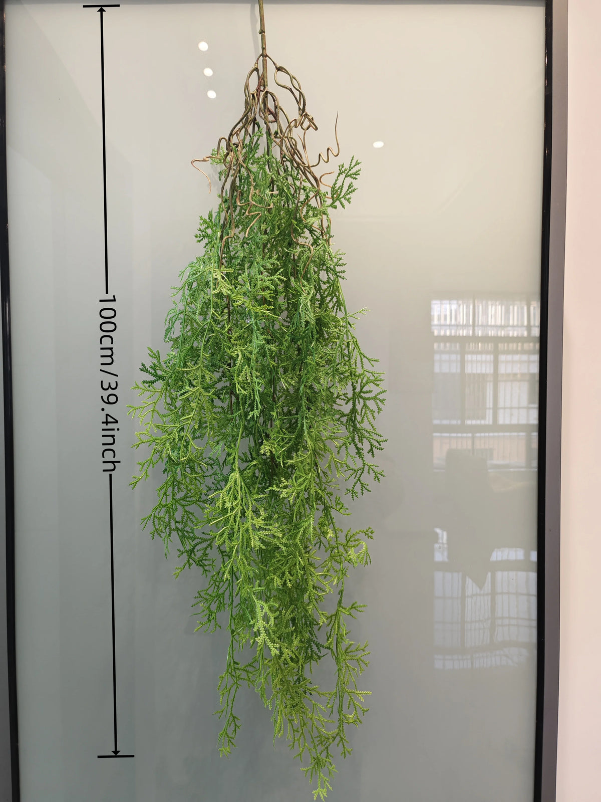Artificial hanging ivy vine with brown tendrils displayed against a glass panel.