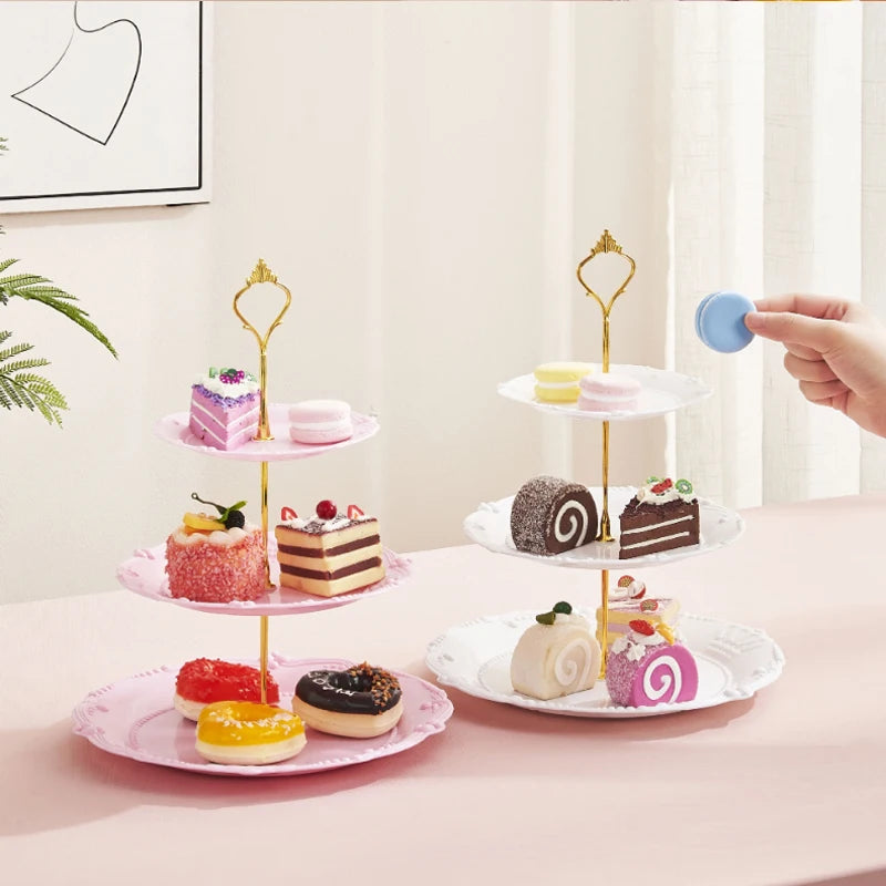 A three-tier plastic cupcake stand with pink and gold accents displaying various cupcakes.