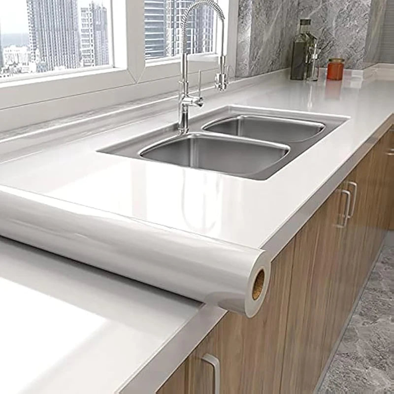 A modern kitchen sink and faucet installed in a white countertop, featuring a marble self-adhesive wallpaper roll.