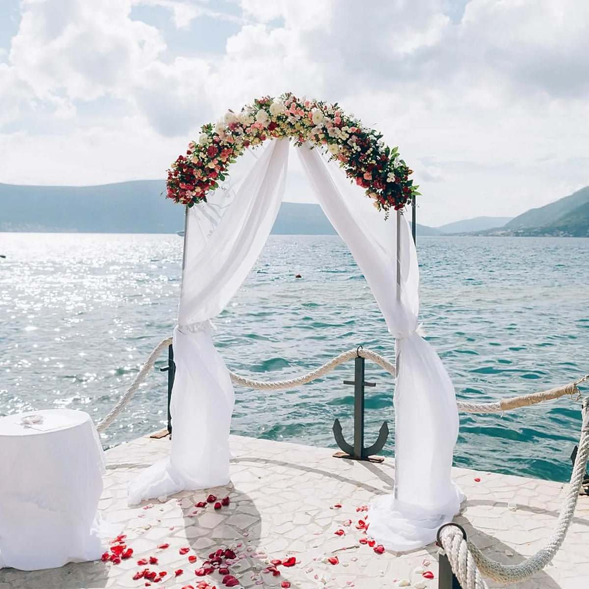 Elegant white chiffon drapes forming an archway over the sea with floral accents.