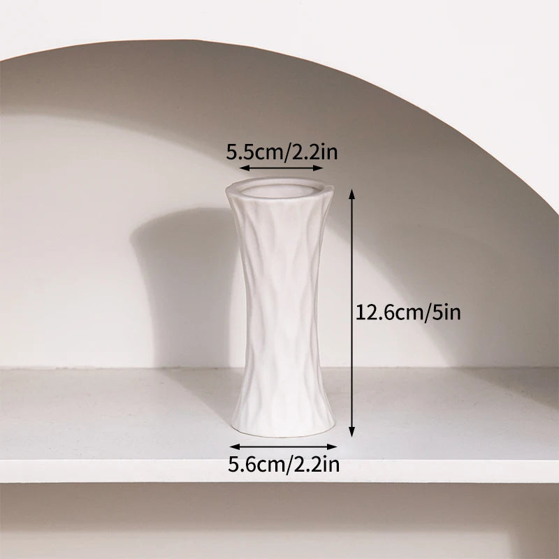A white ceramic bud vase with a tapered shape is displayed on a shelf.