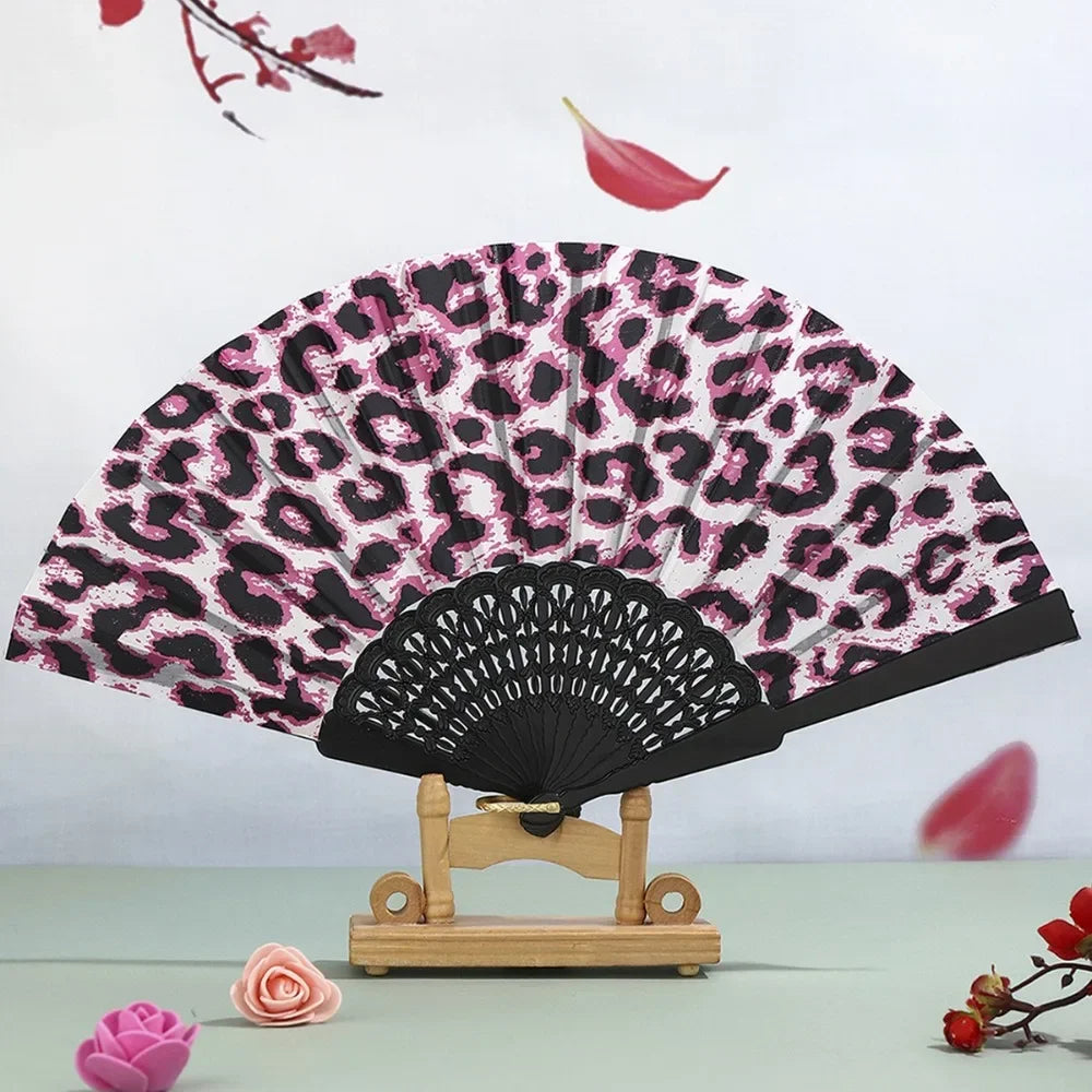 A leopard print folding hand fan with a black handle displayed against a light background.