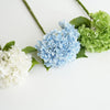 A floral arrangement featuring white and blue hydrangea silk flowers on green stems.