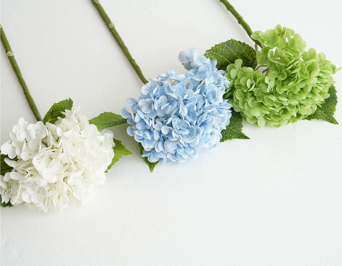 A floral arrangement featuring white and blue hydrangea silk flowers on green stems.
