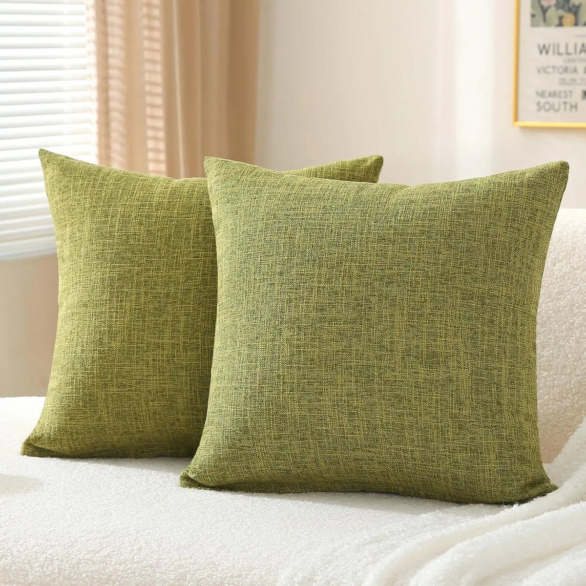 A set of two olive green linen pillows resting on a white textured surface.