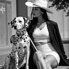 A woman wearing a wide-brimmed hat sits next to a dog, posing for a black and white art print photograph.