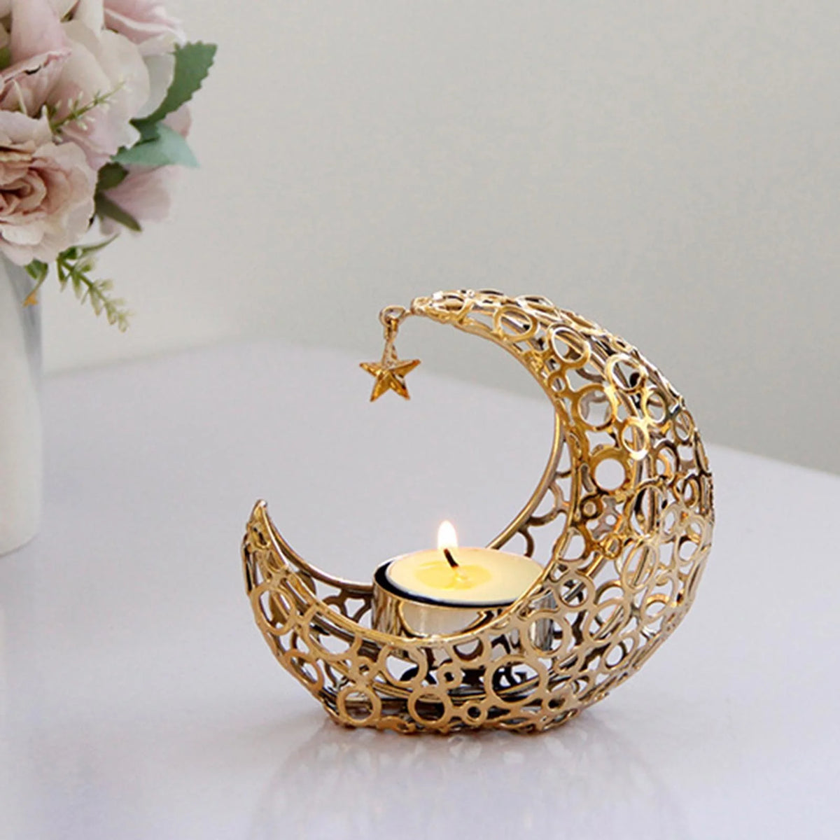 A golden crescent moon candle holder with a star detail sits on a white surface.