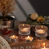 A collection of clear glass tealight candle holders and candles arranged on a wooden surface with natural elements.