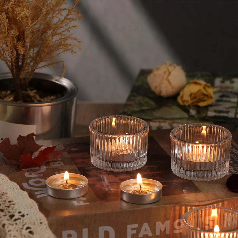 A collection of clear glass tealight candle holders and candles arranged on a wooden surface with natural elements.