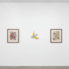 A wall sculpture featuring a lifelike resin banana, displayed on a white gallery wall.