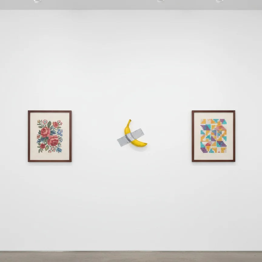 A wall sculpture featuring a lifelike resin banana, displayed on a white gallery wall.