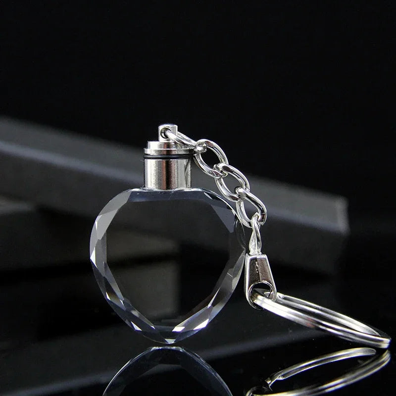 Colgante y cadena de corazón de cristal claro en un set para llavero, mostrados sobre una superficie reflectante.