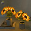 A bright yellow sunflower LED night light with a dark center is displayed in a white ceramic pot.