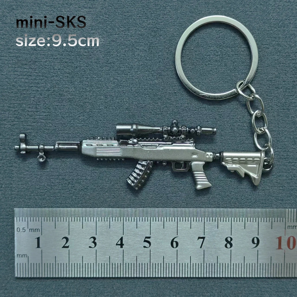 A silver alloy gun model miniature keychain with a realistic finish, shown next to a ruler.