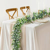 A long garland of artificial eucalyptus vine with white flowers decorates a table setting.