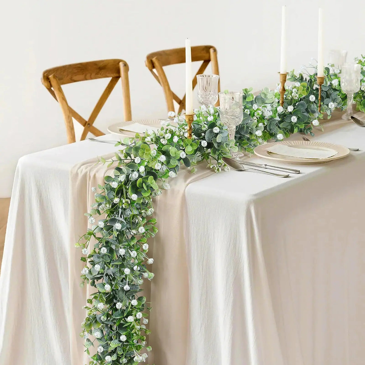 A long garland of artificial eucalyptus vine with white flowers decorates a table setting.