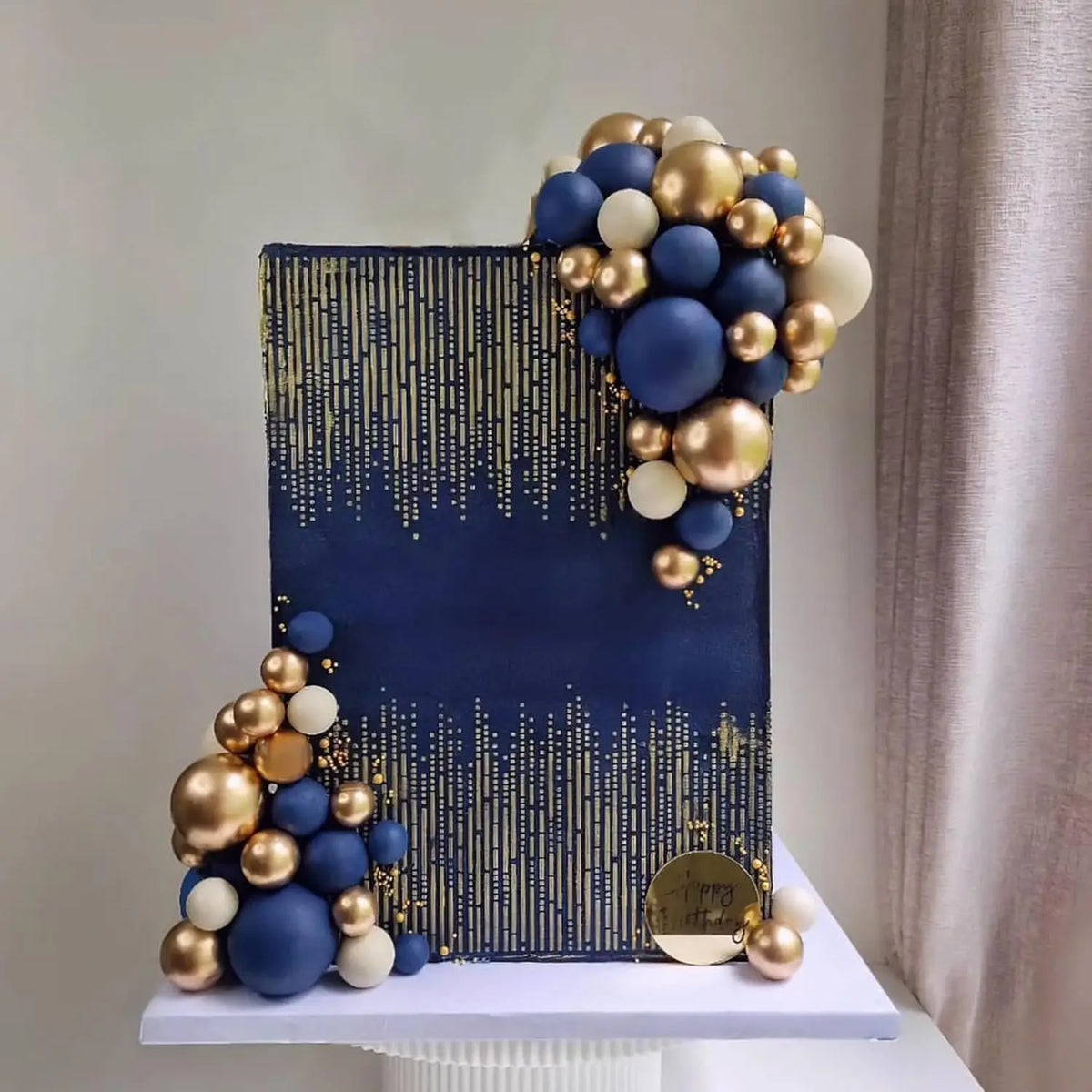 A set of blue, white, and gold ball cake toppers displayed on a dark blue square background.