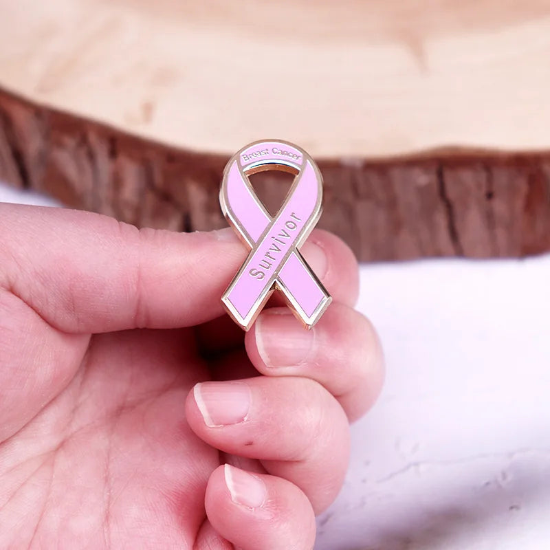 Una mano sostiene un broche de esmalte rosa de concienciación sobre el cáncer de mama contra un fondo de madera.