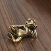 A small antique brass sculpture of a frog in a crouching pose on a dark wooden surface.