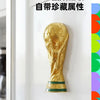 A gold-colored FIFA World Cup trophy fridge magnet displayed on a white surface.