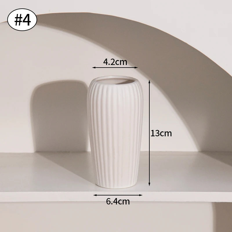 A white ceramic bud vase with vertical ridges is displayed on a shelf.