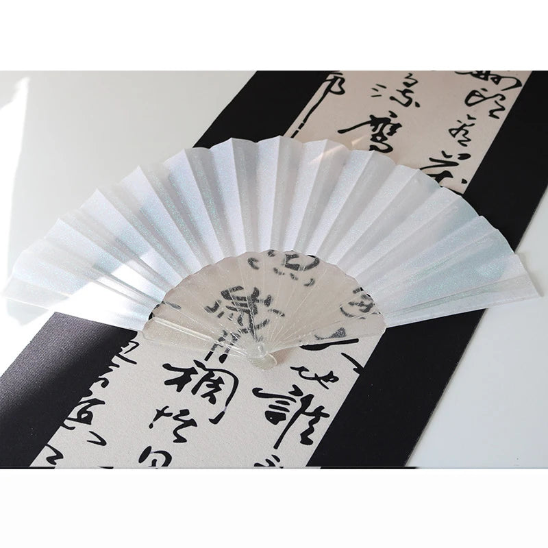 A white glitter folding fan with transparent ribs is displayed against a black background and traditional Japanese text.