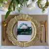 Elegant gold charger plates set on a linen napkin with greenery and white roses.