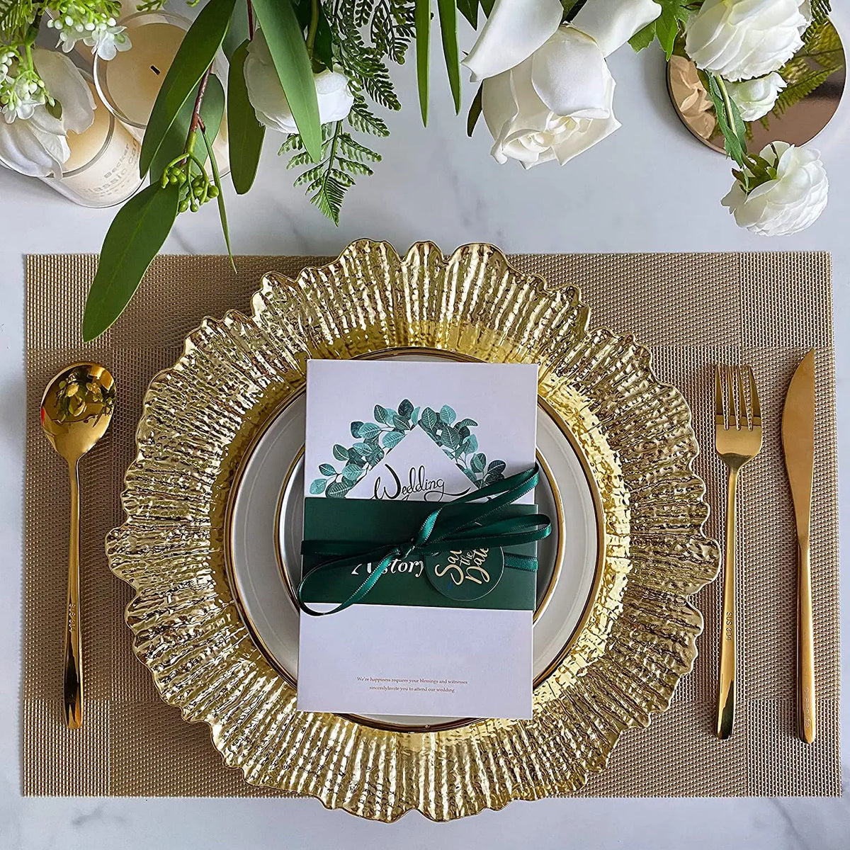 Elegant gold charger plates set on a linen napkin with greenery and white roses.