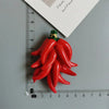 A cluster of bright red chili peppers with green stems placed on a ruler.