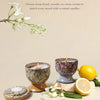 A set of scented candles and a lemon, displayed with white flowers and greenery.
