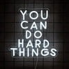 A white neon sign on a dark background reads You Can Do Hard Things.