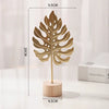 A golden ginkgo leaf metal decorative sculpture standing on a wooden base.