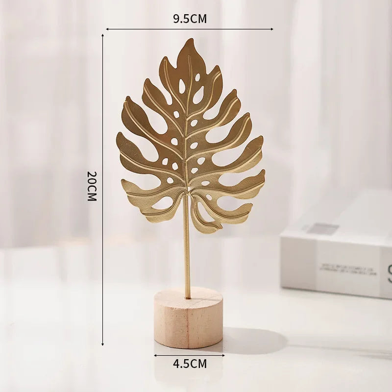 A golden ginkgo leaf metal decorative sculpture standing on a wooden base.