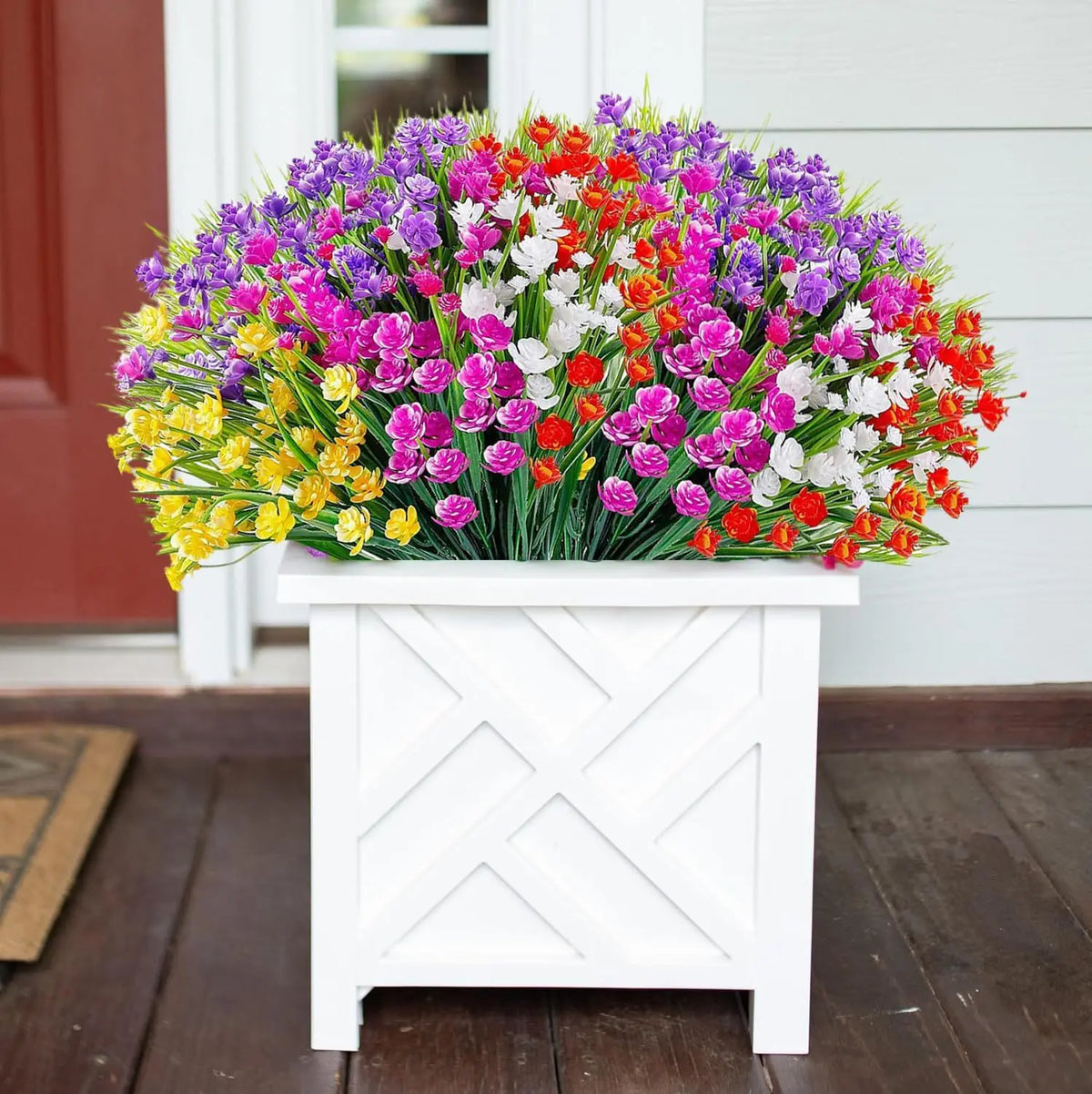 A vibrant bouquet of mixed artificial flowers in purple, pink, white, and orange on a white wooden planter.