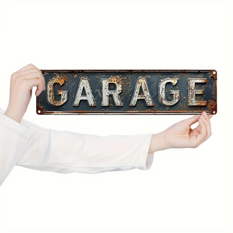 A hand holds up a vintage, weathered metal sign with the word GARAGE engraved on it.