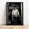 Black and white photograph of a man sitting in a dark setting, framed as wall art.