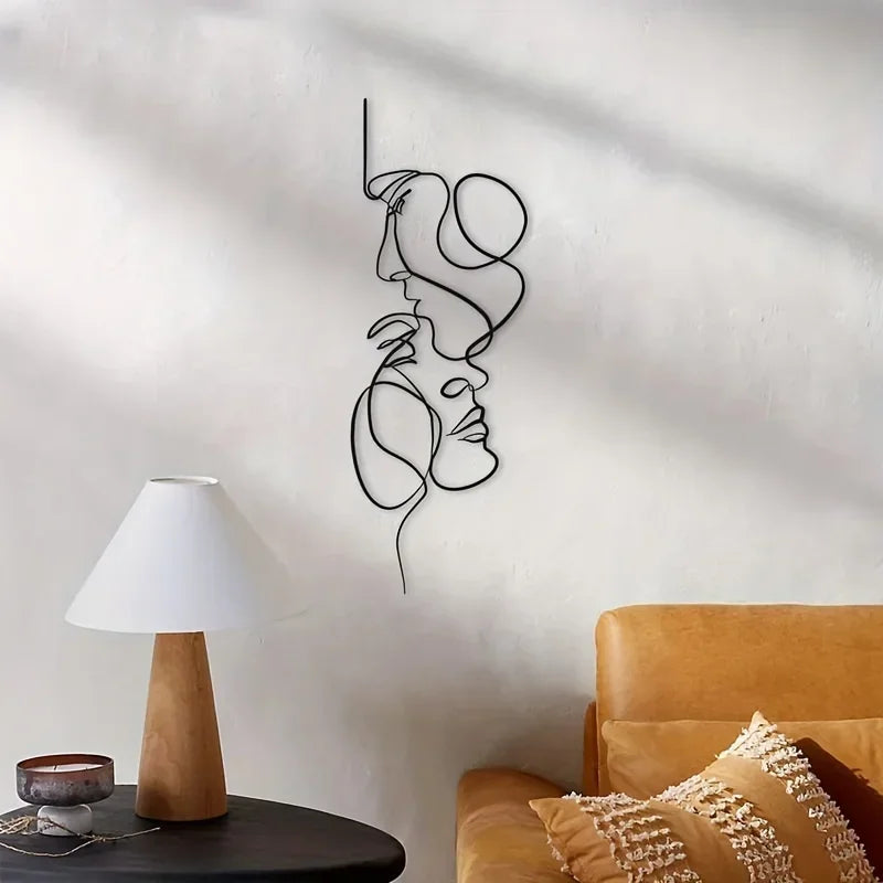 Black line minimalist abstract face metal wall art hanging on a white wall next to a lamp and leather furniture.
