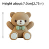 A small, light brown cartoon teddy bear figure with a green bow and white accents.