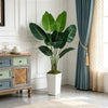 Artificial Bird of Paradise plant in a white planter displayed on a wooden cabinet next to a window.