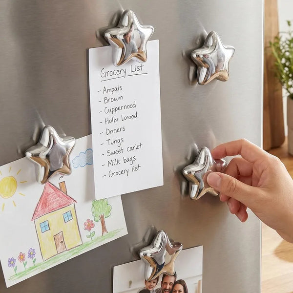 A hand is placing a star-shaped magnetic photo clip onto a stainless steel refrigerator surface next to a grocery list.