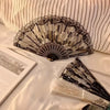 An elegant lace rose folding fan with black and white detailing is displayed on a white surface.