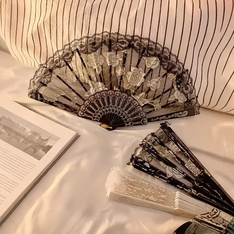 An elegant lace rose folding fan with black and white detailing is displayed on a white surface.