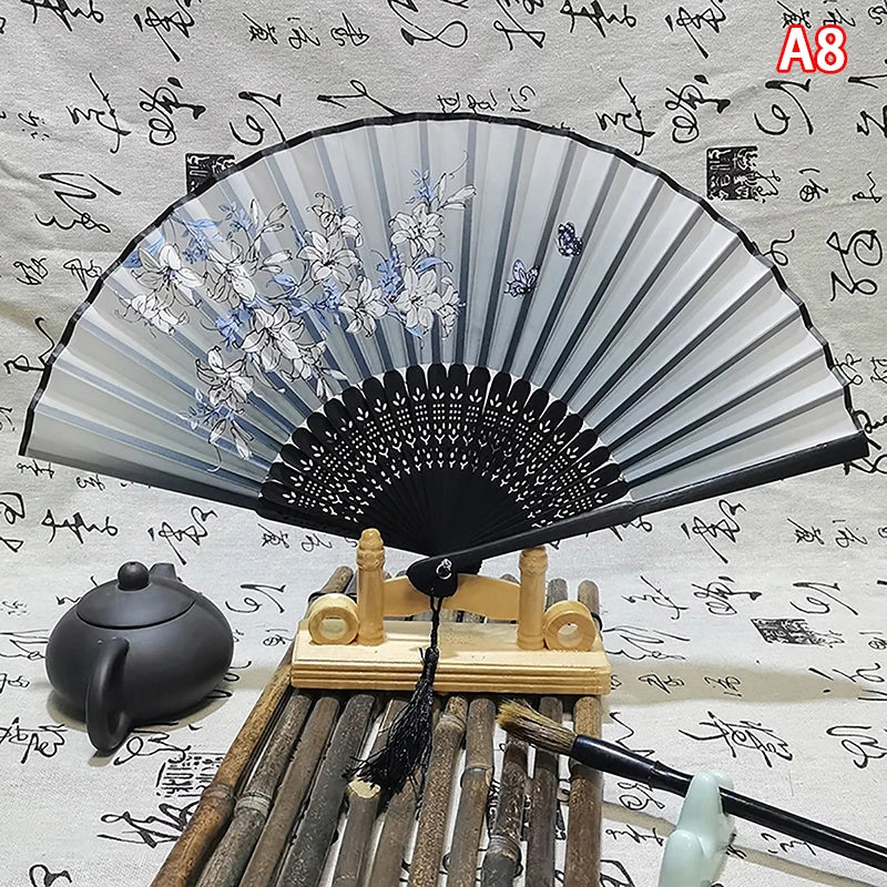 An elegant vintage Chinese folding hand fan with grey and white floral patterns displayed on a wooden stand.